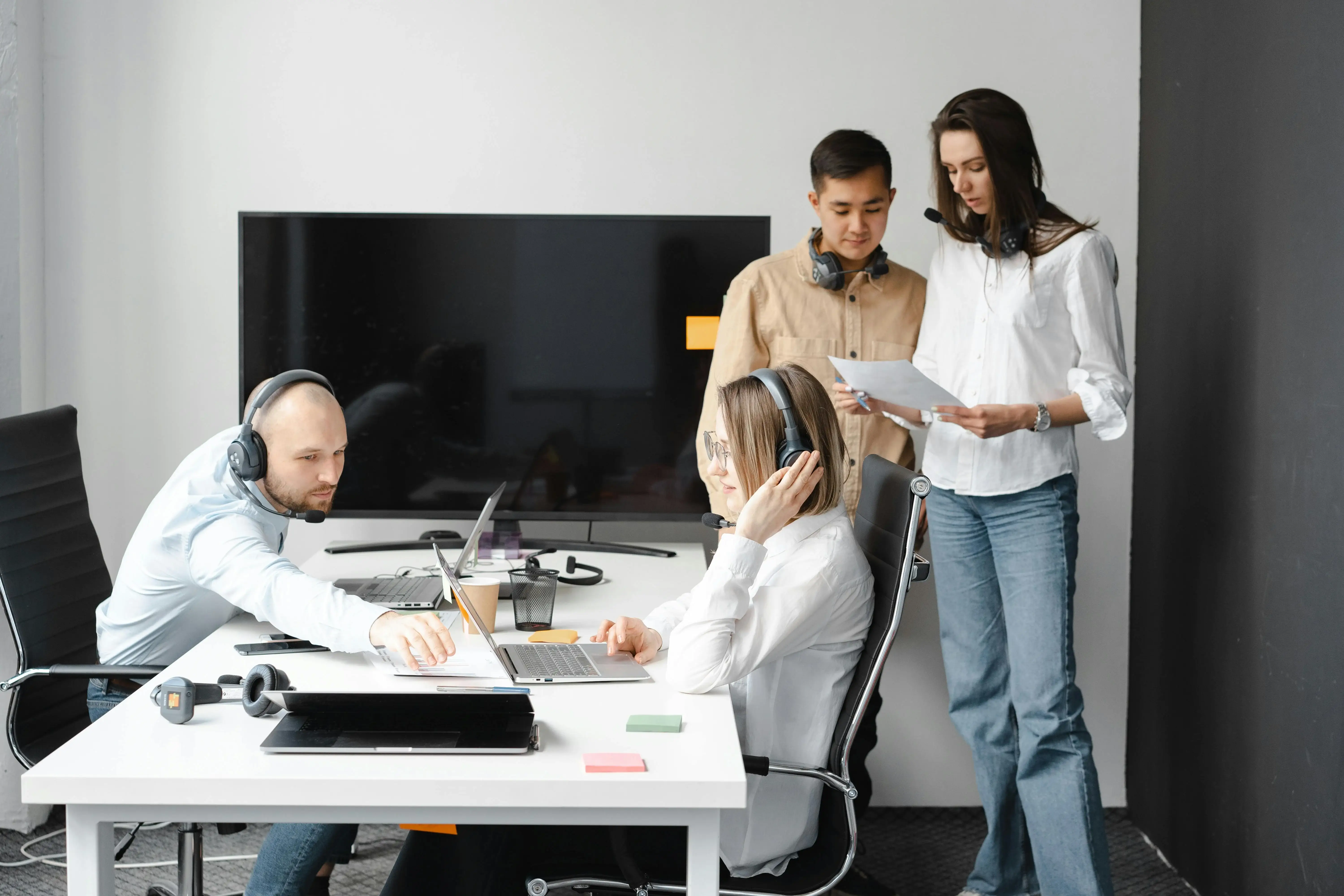 A dedicated IT support team with headphones working collaboratively on laptops in a modern office, symbolizing responsive technical assistance and operational management.